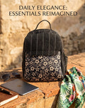 A textured woven backpack featuring a prominent floral patterned lower half, displayed alongside a tablet, sunglasses, and a leafy-print scarf on an outdoor ledge.