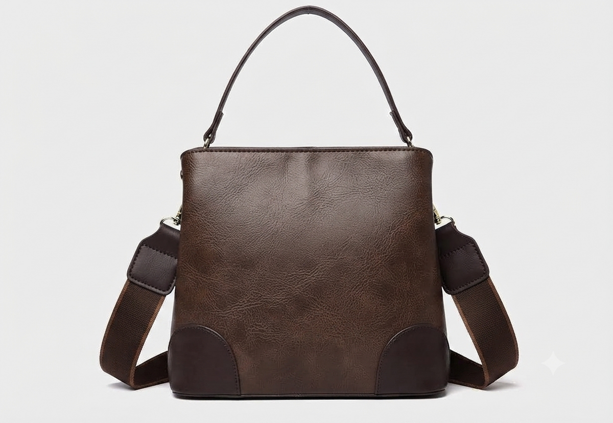A structured faux-leather handbag featuring a large, central circular bronze plate embossed with an intricate royal Indian design, finished with a slim top handle and a thick brown adjustable strap.