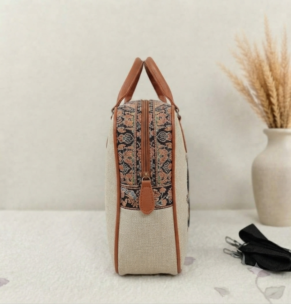 A structured canvas travel duffle bag featuring a detailed traditional Indian royal elephant motif, accented with brown top handles and complete with a detachable shoulder strap.