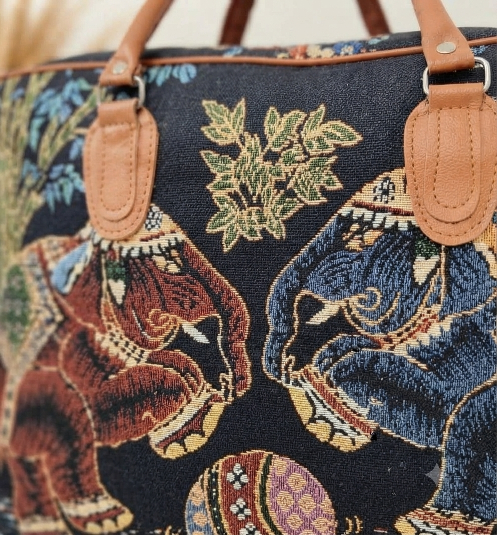 A structured canvas travel duffle bag featuring a detailed traditional Indian royal elephant motif, accented with brown top handles and complete with a detachable shoulder strap.