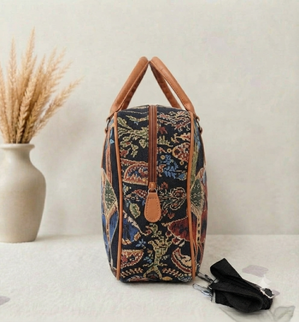 A structured canvas travel duffle bag featuring a detailed traditional Indian royal elephant motif, accented with brown top handles and complete with a detachable shoulder strap.