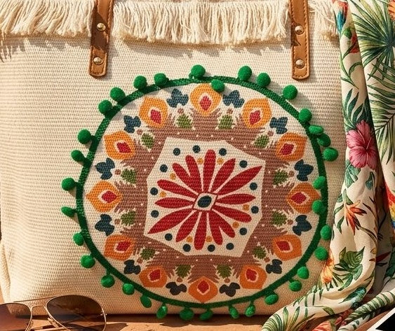 A large canvas tote bag featuring an embroidered geometric mandala circular design on the front panel with a fringed trim along the top rim and leather shoulder handles.