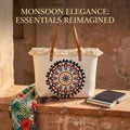 A large canvas tote bag featuring an embroidered geometric mandala circular design on the front panel with a fringed trim along the top rim and leather shoulder handles.