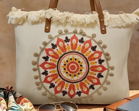 A large canvas tote bag featuring an embroidered geometric mandala circular design on the front panel with a fringed trim along the top rim and leather shoulder handles.