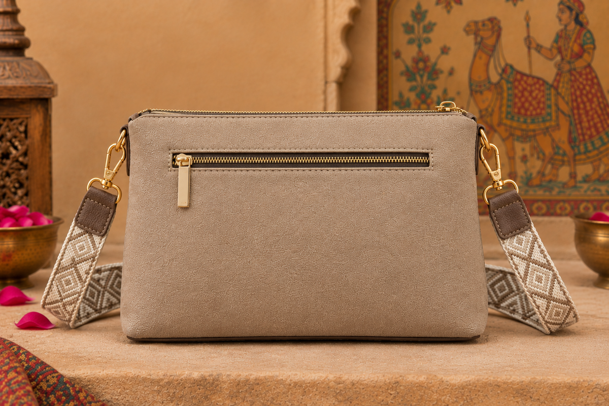 A suede multi-pocket sling bag with a circular embossed center emblem and an adjustable patterned crossbody strap.