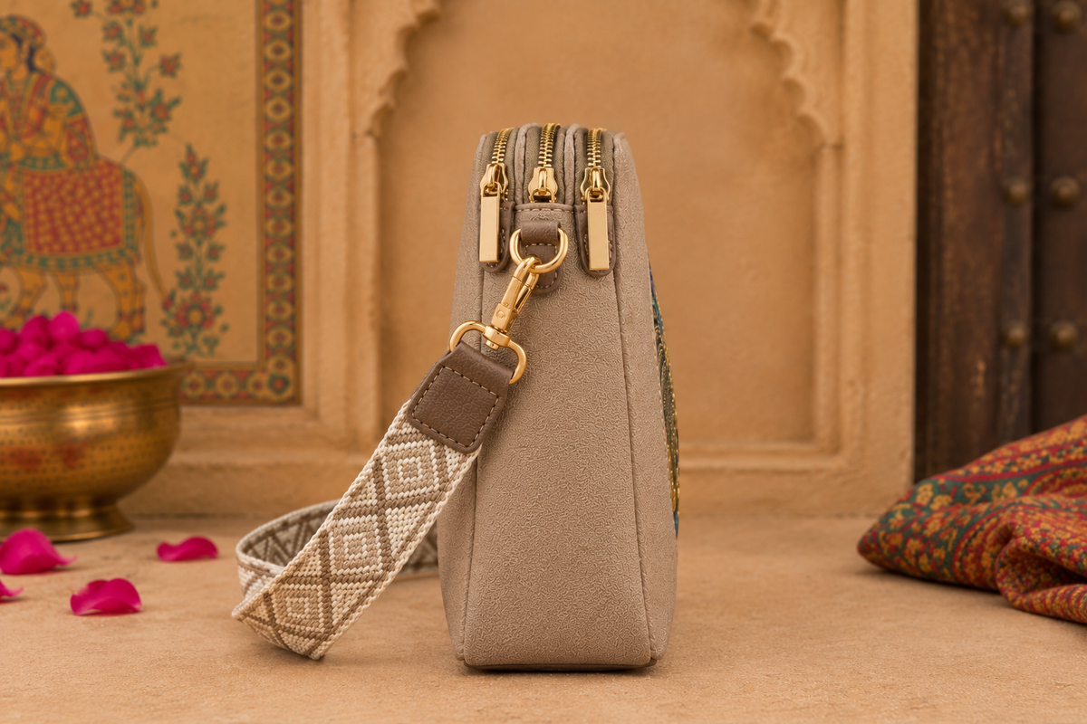 A suede multi-pocket sling bag with a circular embossed center emblem and an adjustable patterned crossbody strap.