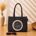 A structured rectangular canvas satchel handbag featuring an intricate circular fringed emblem with an artisanal motif, accented by contrast top handles and a matching detachable shoulder strap.