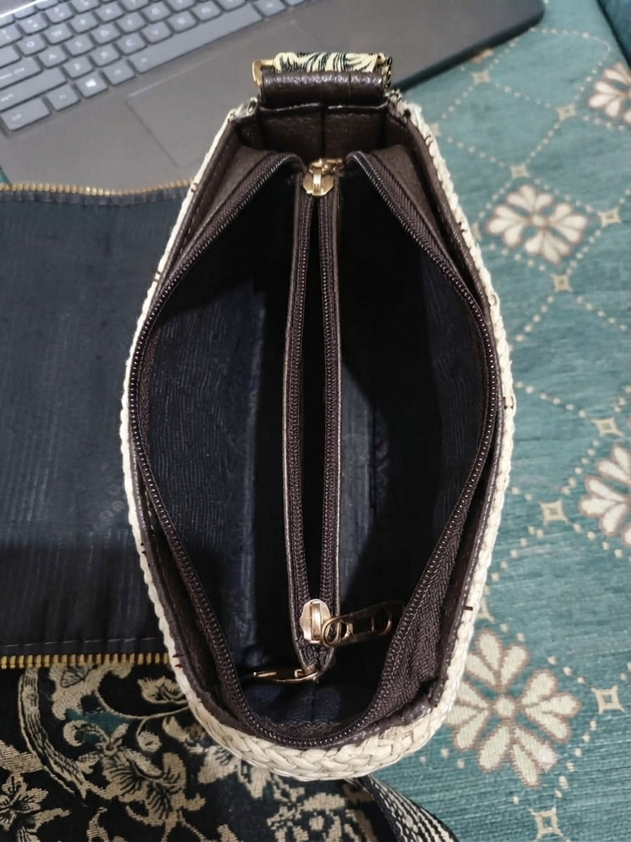 An overhead view showing the open interior of a beige straw-woven crossbody sling bag, revealing a dark brown fabric lining divided into two main sections by a central zippered compartment.